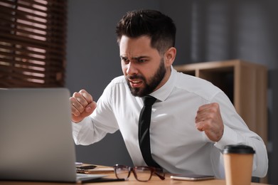 Emotional young businessman working on laptop in office. Online hate concept Photo of Emotional young businessman working on laptop in office. Online hate concept
