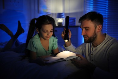 Father with little daughter reading fairy tale in dark bedroom Photo of Father with little daughter reading fairy tale in dark bedroom