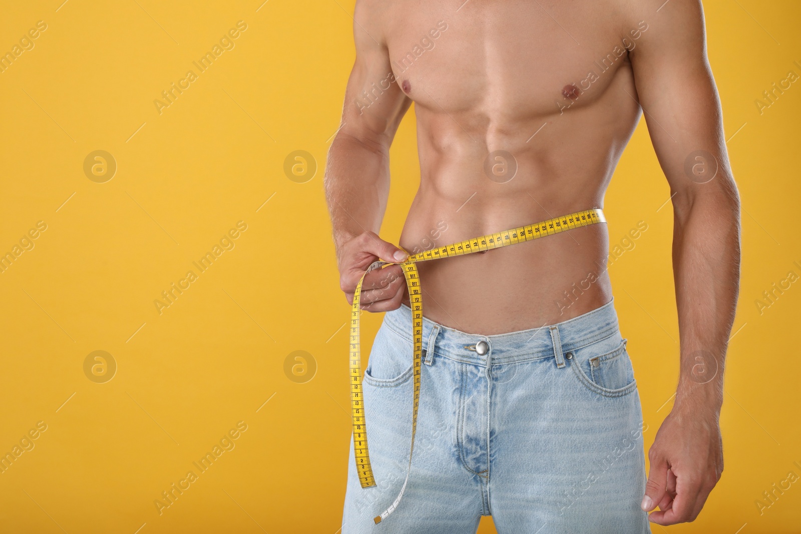 Shirtless man with slim body and measuring tape around his waist on yellow background, closeup. Space for text Photo of Shirtless man with slim body and measuring tape around his waist on yellow background, closeup. Space for text