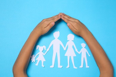 Child covering paper family figures with hands on light blue background, top view Photo of Child covering paper family figures with hands on light blue background, top view