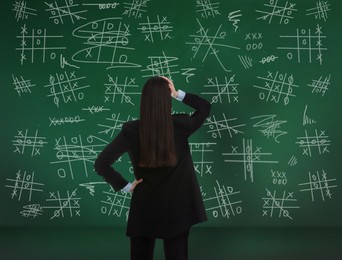 Young businesswoman near green chalkboard with drawn tic tac toe game, back view Image of Young businesswoman near green chalkboard with drawn tic tac toe game, back view