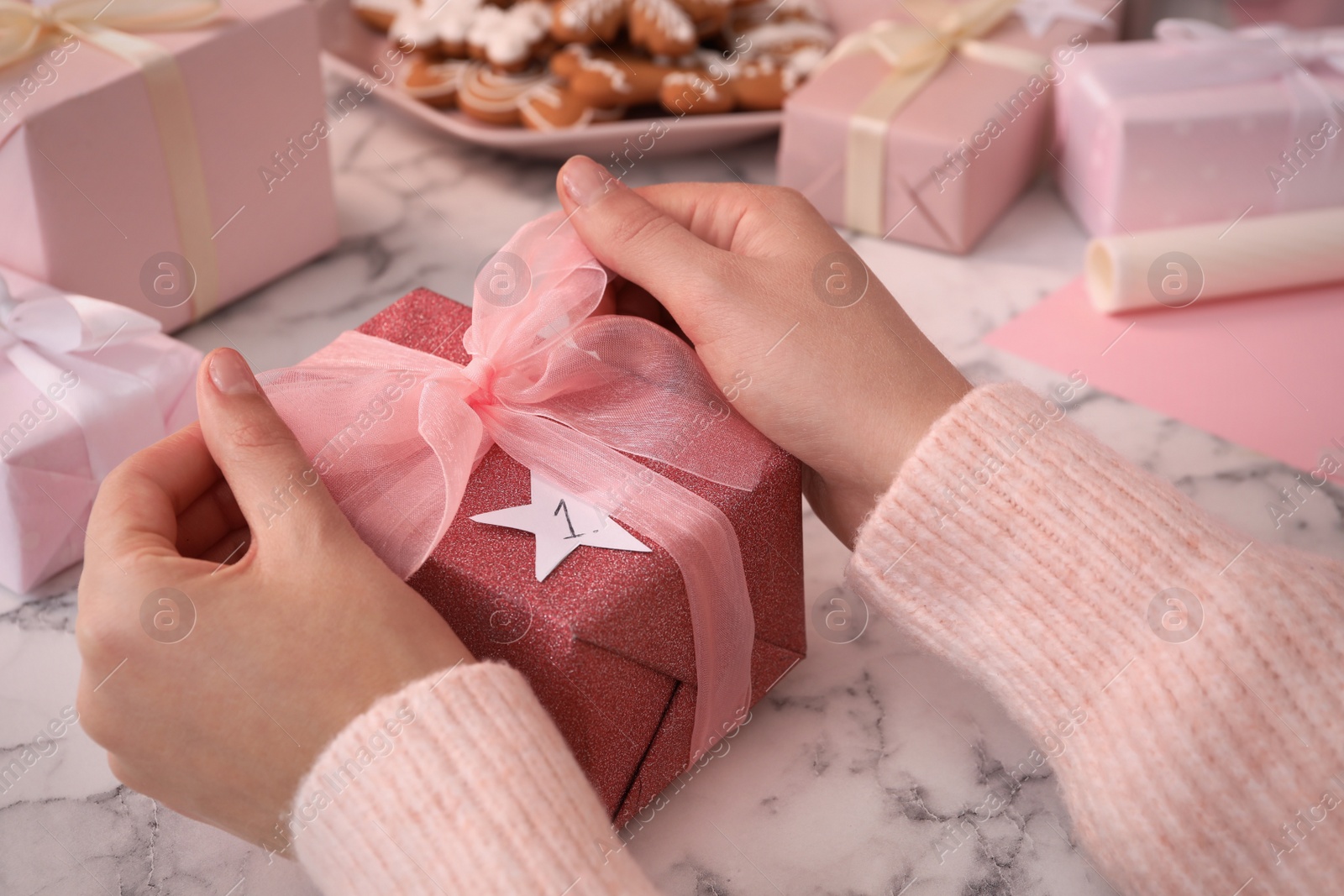 Woman with gift box at white marble table, closeup. Creating advent calendar Photo of Woman with gift box at white marble table, closeup. Creating advent calendar