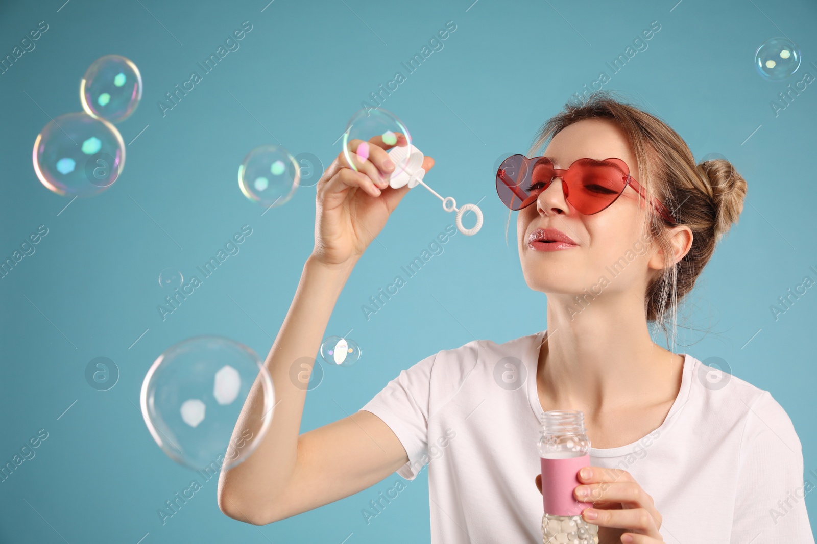 Young woman blowing soap bubbles on light blue background Photo of Young woman blowing soap bubbles on light blue background