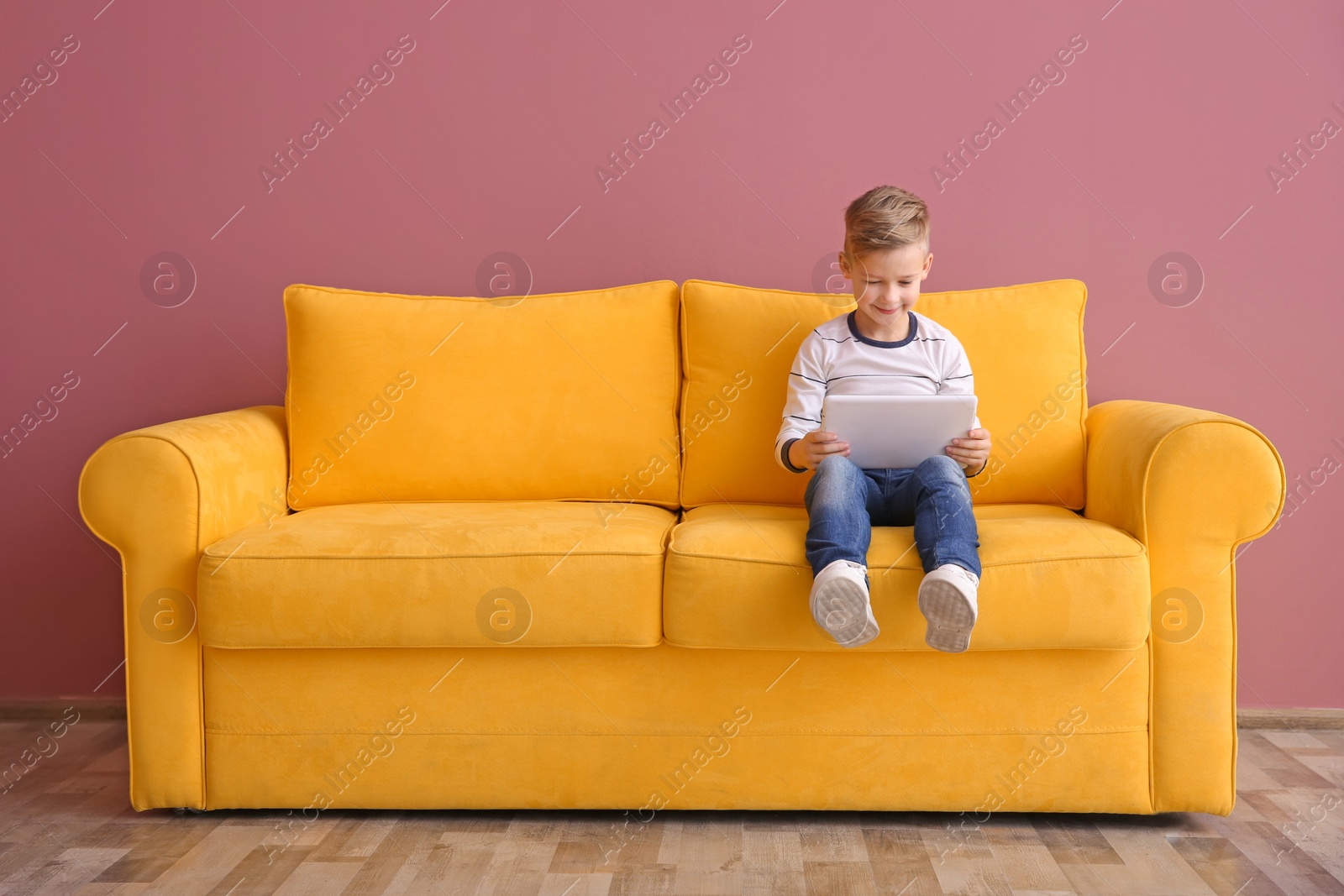 Cute little boy sitting on sofa with tablet computer, indoors Photo of Cute little boy sitting on sofa with tablet computer, indoors