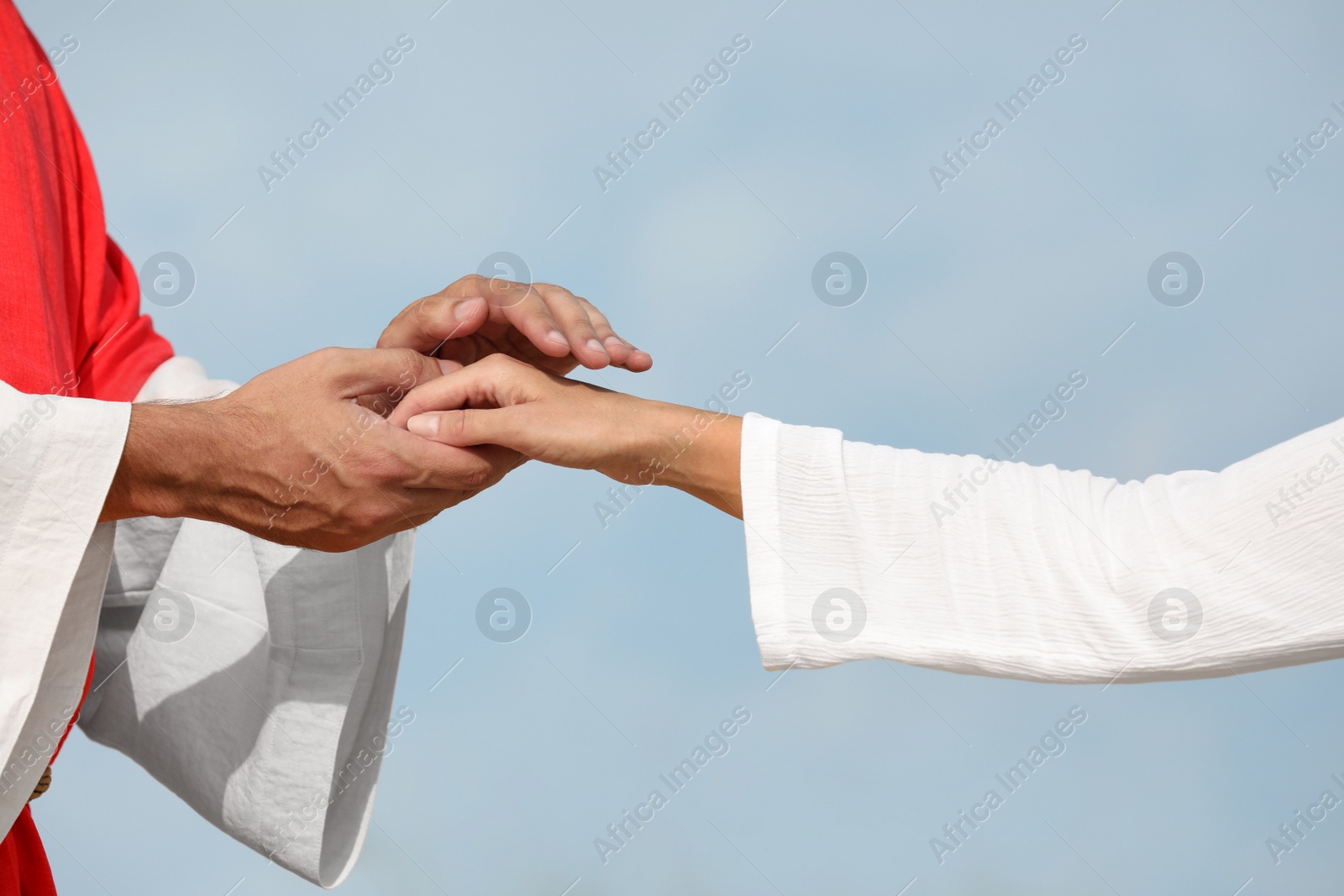 Jesus Christ holding woman's hand against blue sky, closeup Photo of Jesus Christ holding woman's hand against blue sky, closeup