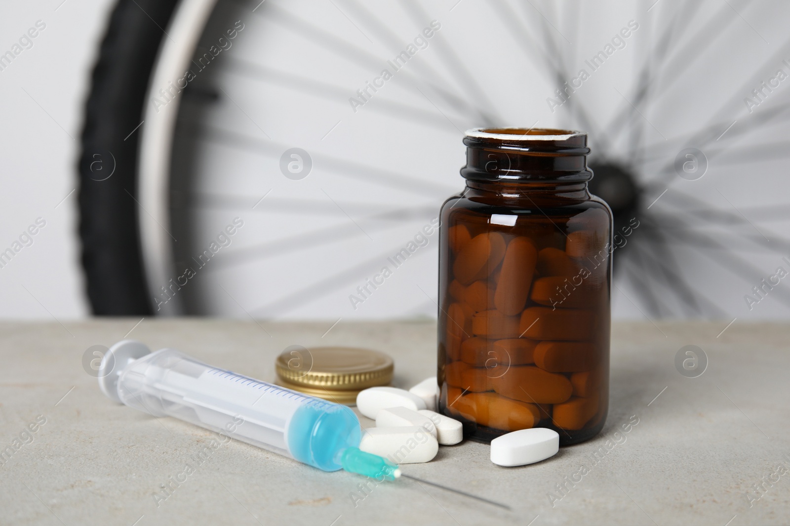 Pills and syringe on light grey table near bike wheel. Using doping in cycling sport concept Photo of Pills and syringe on light grey table near bike wheel. Using doping in cycling sport concept
