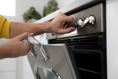 Photo of Man using modern oven in kitchen, closeup