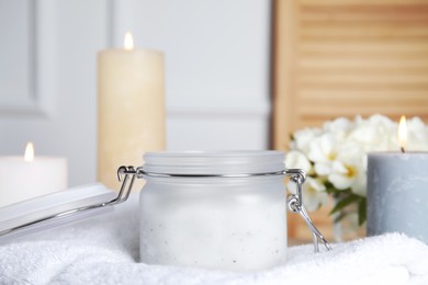 Jar of natural exfoliating salt scrub on white towel Photo of Jar of natural exfoliating salt scrub on white towel