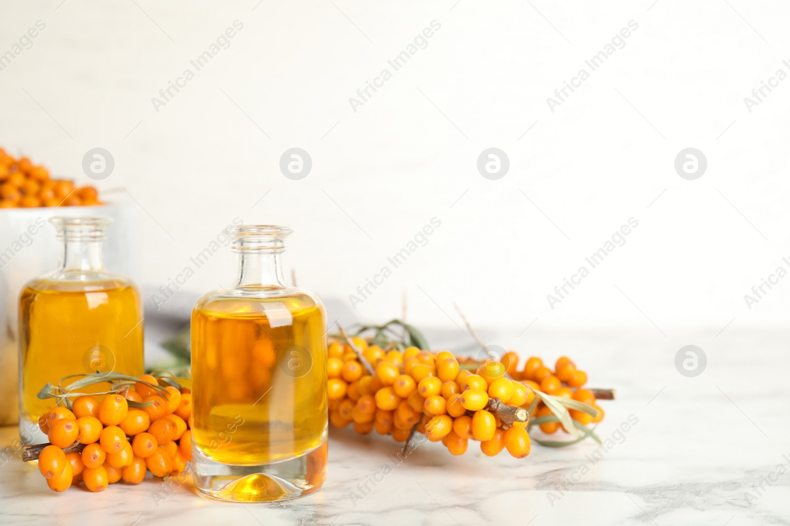 Natural sea buckthorn oil and fresh berries on white marble table. Space for text Photo of Natural sea buckthorn oil and fresh berries on white marble table. Space for text