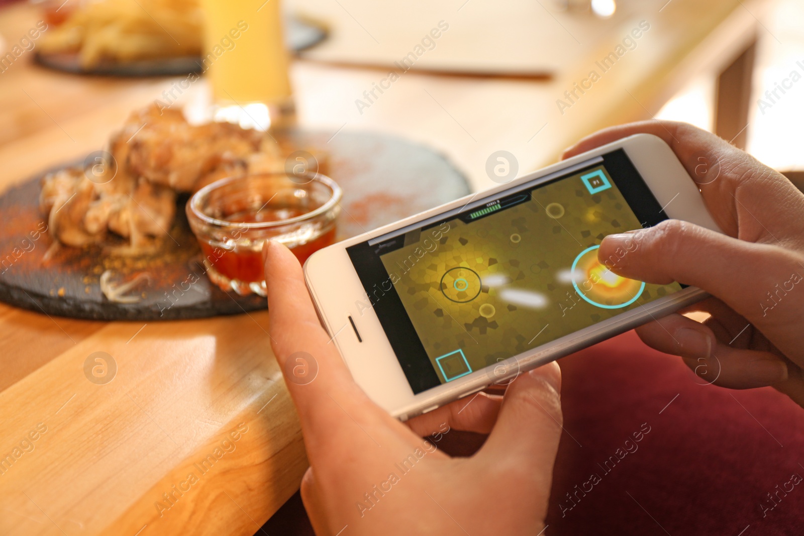 Woman playing game using smartphone at table with tasty BBQ wings in cafe, closeup Photo of Woman playing game using smartphone at table with tasty BBQ wings in cafe, closeup