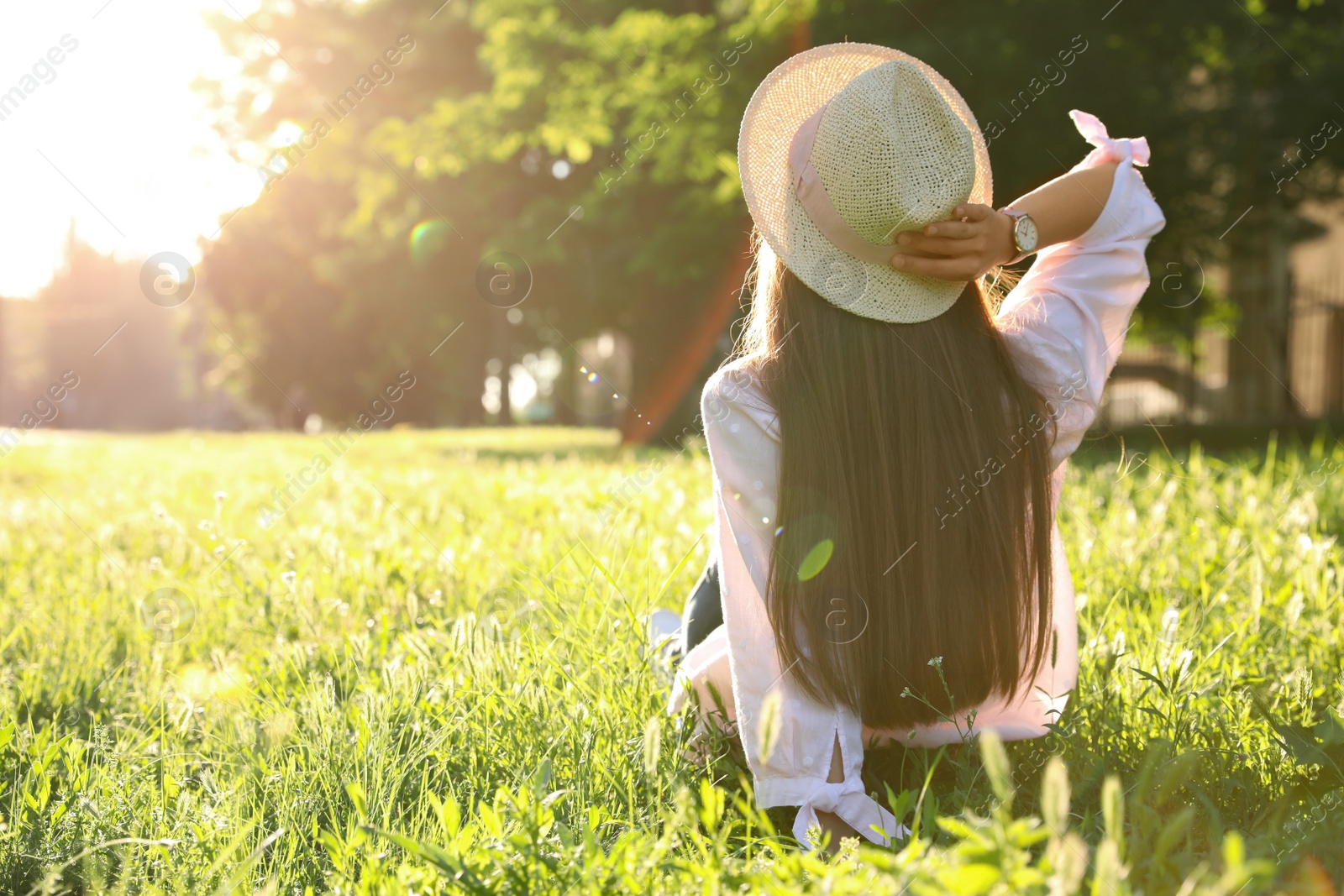 Young woman in straw hat sitting outdoors on sunny day, back view Photo of Young woman in straw hat sitting outdoors on sunny day, back view