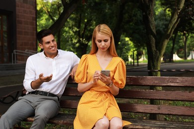 Young woman with smartphone ignoring her boyfriend in park. Boring date Photo of Young woman with smartphone ignoring her boyfriend in park. Boring date