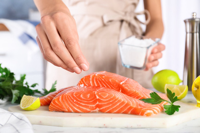 Woman salting fresh raw salmon at table, closeup. Fish delicacy Photo of Woman salting fresh raw salmon at table, closeup. Fish delicacy
