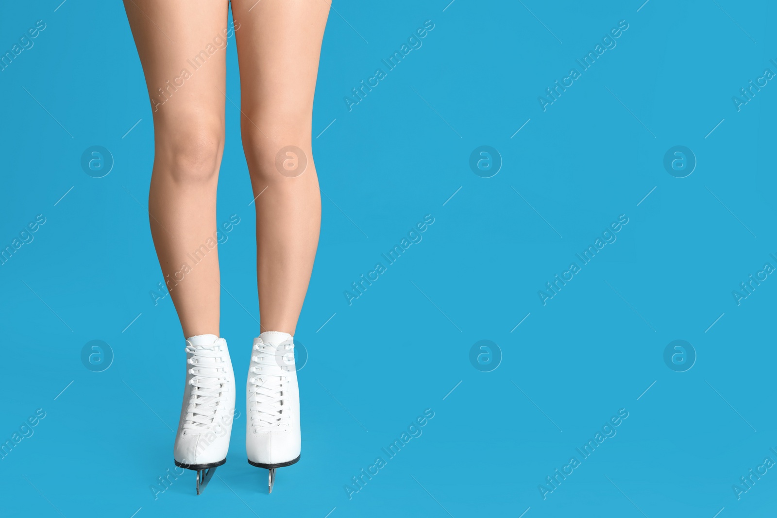 Photo of Woman in elegant white ice skates on light blue background, closeup of legs. Space for text