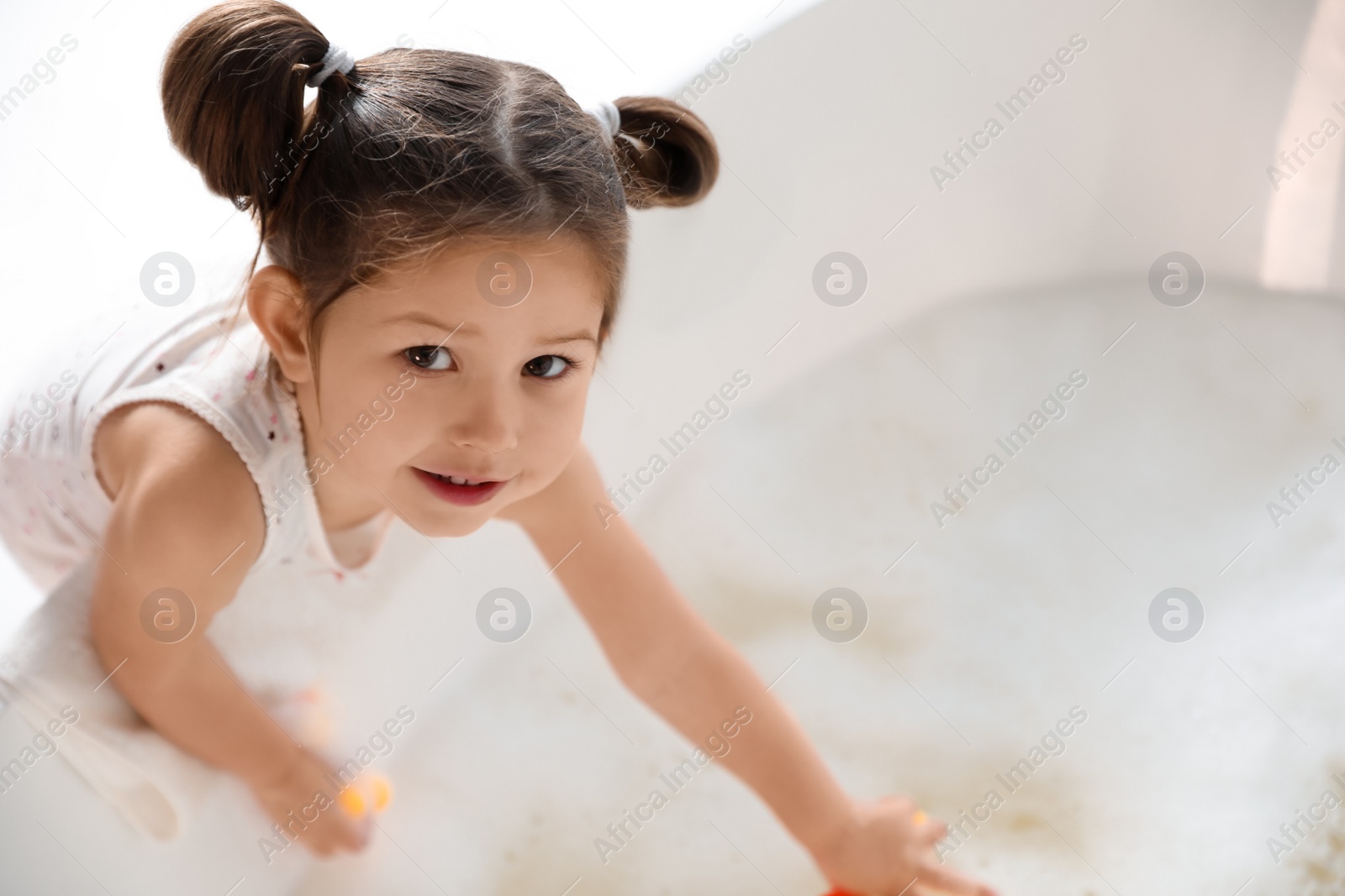 Photo of Cute little girl near tub in bathroom. Space for text