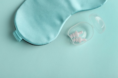 Pair of ear plugs in case and sleeping mask on turquoise background, flat lay Photo of Pair of ear plugs in case and sleeping mask on turquoise background, flat lay