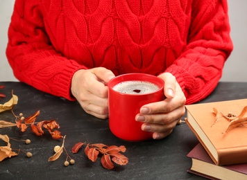 Woman with cup of hot drink at black table, closeup. Cozy autumn atmosphere Photo of Woman with cup of hot drink at black table, closeup. Cozy autumn atmosphere