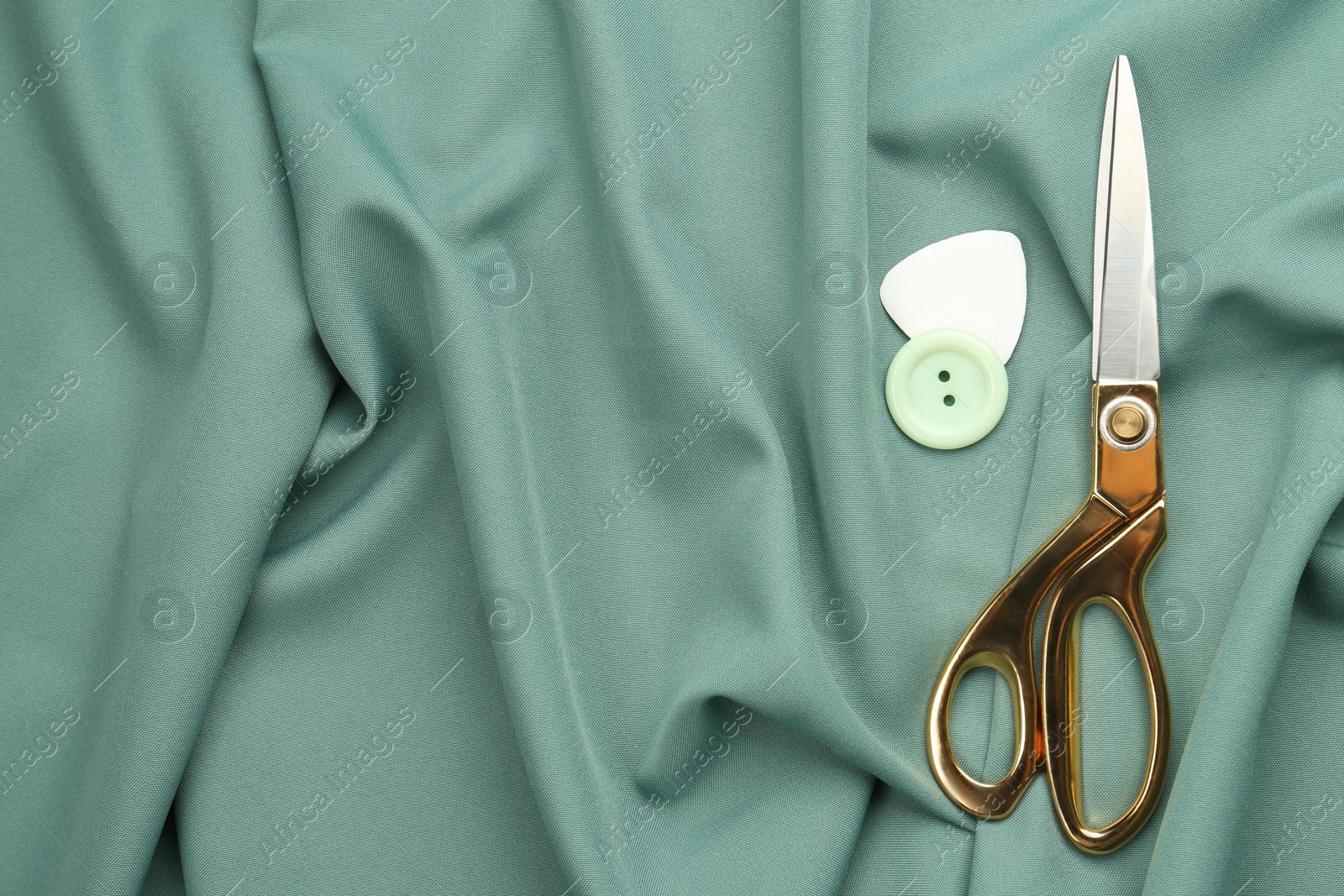 Scissors, button and tailor's chalk on green fabric, flat lay. Space for text Photo of Scissors, button and tailor's chalk on green fabric, flat lay. Space for text