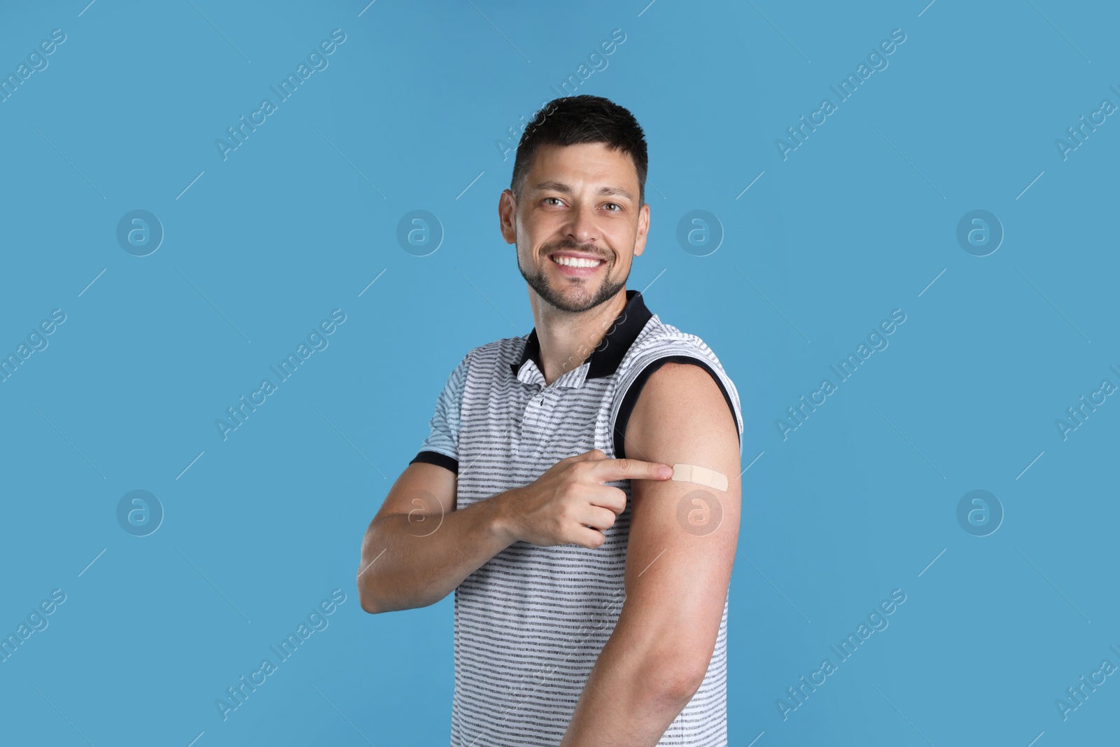 Vaccinated man showing medical plaster on his arm against light blue background Photo of Vaccinated man showing medical plaster on his arm against light blue background
