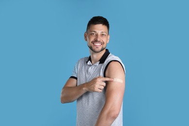 Vaccinated man showing medical plaster on his arm against light blue background Photo of Vaccinated man showing medical plaster on his arm against light blue background