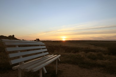 Wooden bench in field at sunrise. Early morning landscape Photo of Wooden bench in field at sunrise. Early morning landscape