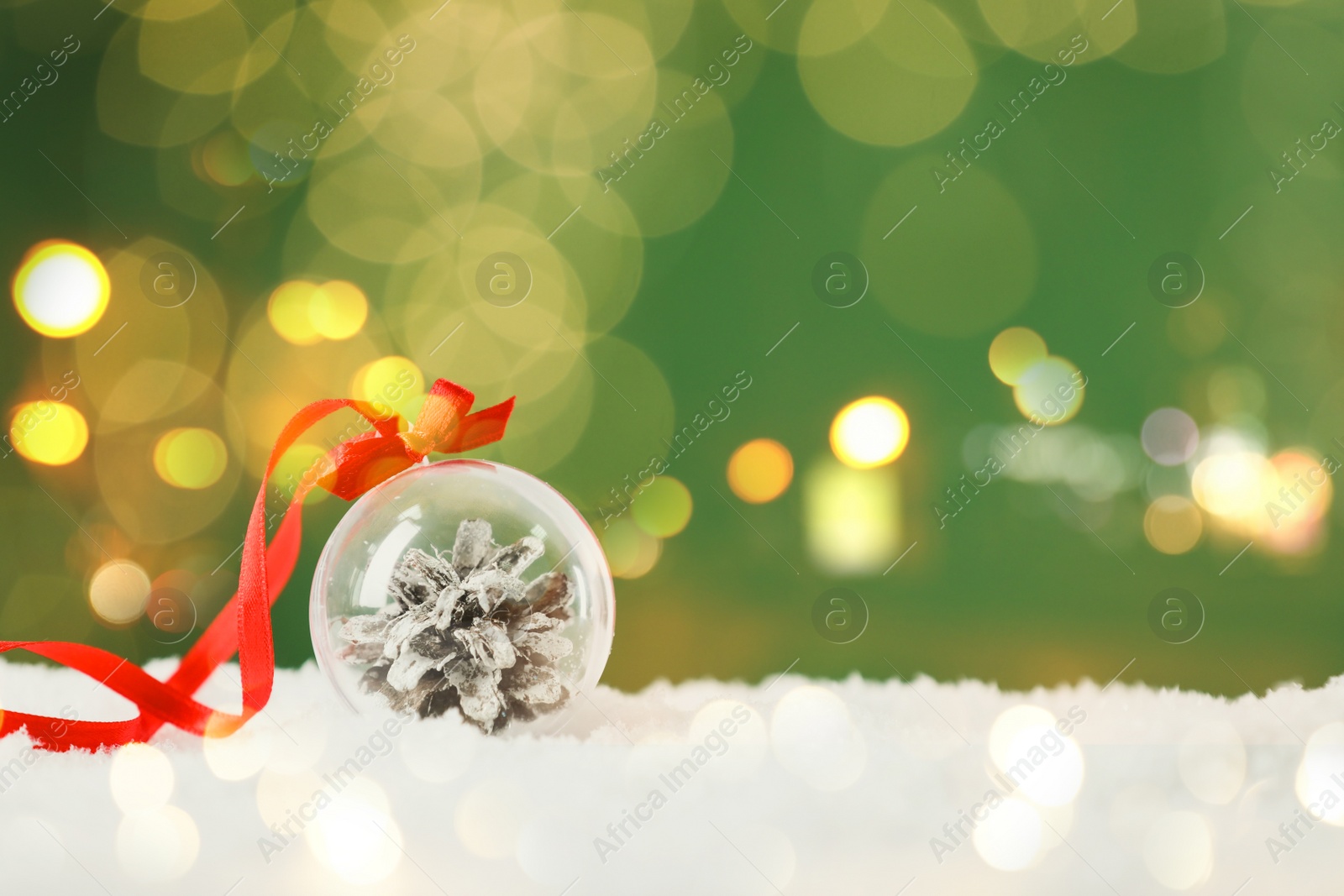 Beautiful transparent Christmas ornament with fir cone on snow against green background, bokeh effect. Space for text Image of Beautiful transparent Christmas ornament with fir cone on snow against green background, bokeh effect. Space for text