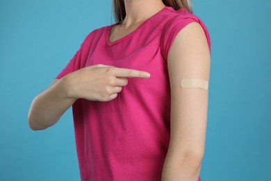Vaccinated woman showing medical plaster on her arm against light blue background, closeup Photo of Vaccinated woman showing medical plaster on her arm against light blue background, closeup