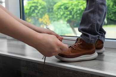 Mother helping son to tie shoe laces near window at home, closeup Photo of Mother helping son to tie shoe laces near window at home, closeup