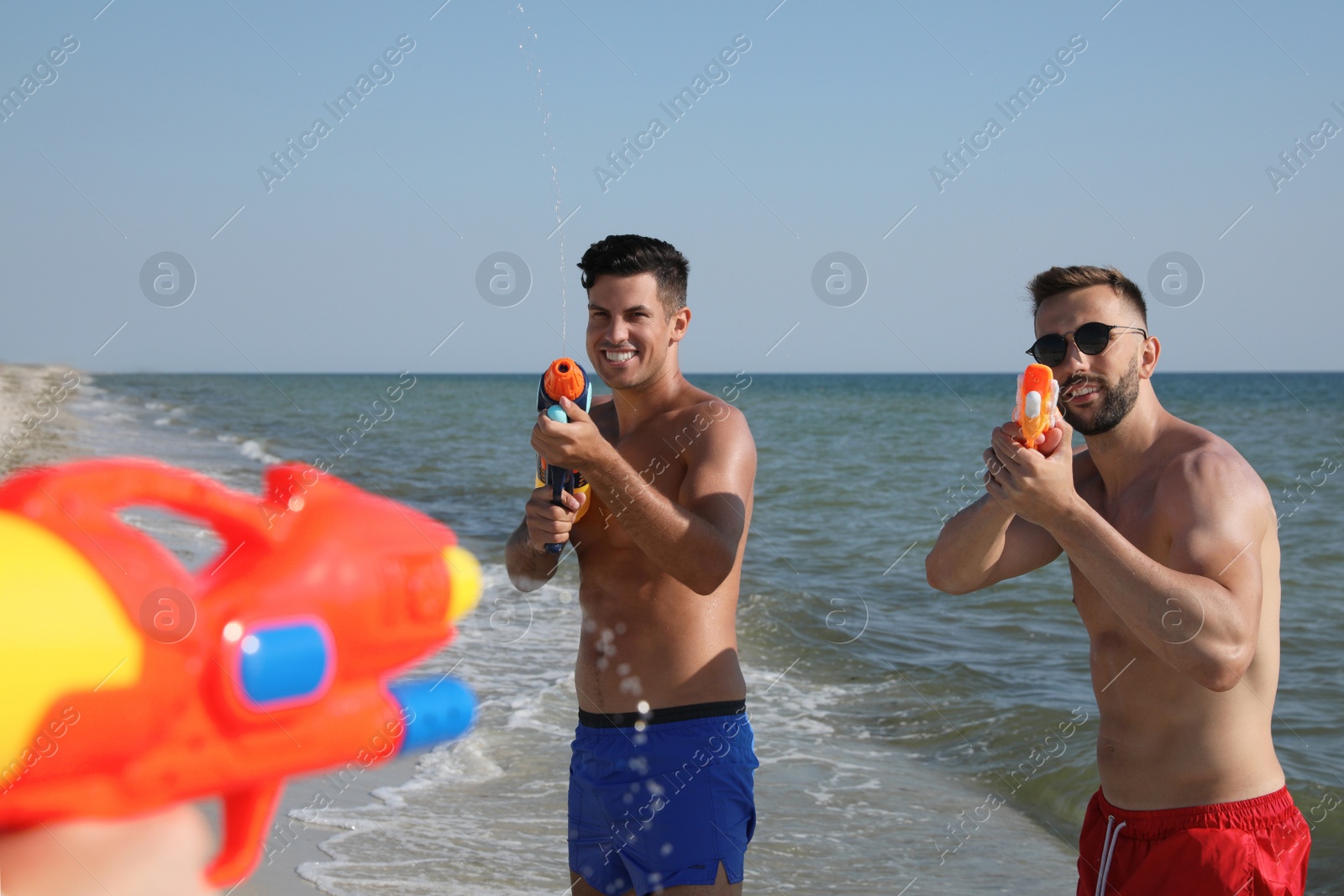Friends with water guns having fun on beach Photo of Friends with water guns having fun on beach