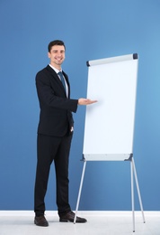 Business trainer giving presentation on flip chart board against color wall background Photo of Business trainer giving presentation on flip chart board against color wall background