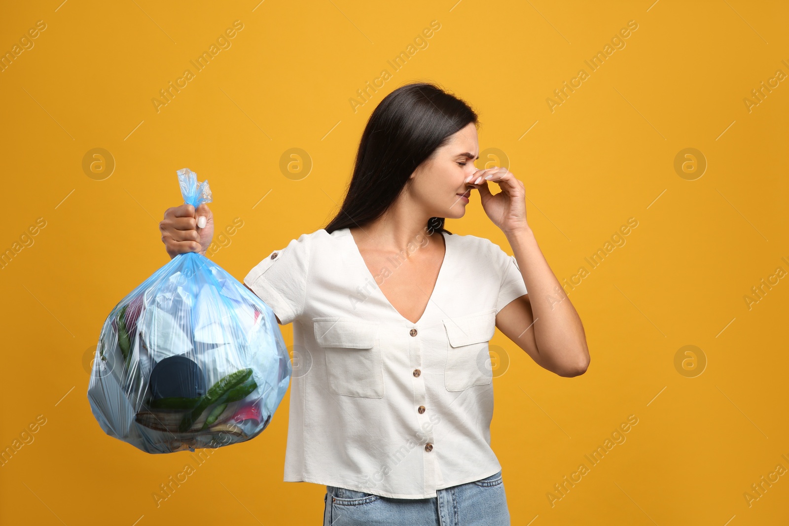 Woman holding full garbage bag on yellow background Photo of Woman holding full garbage bag on yellow background