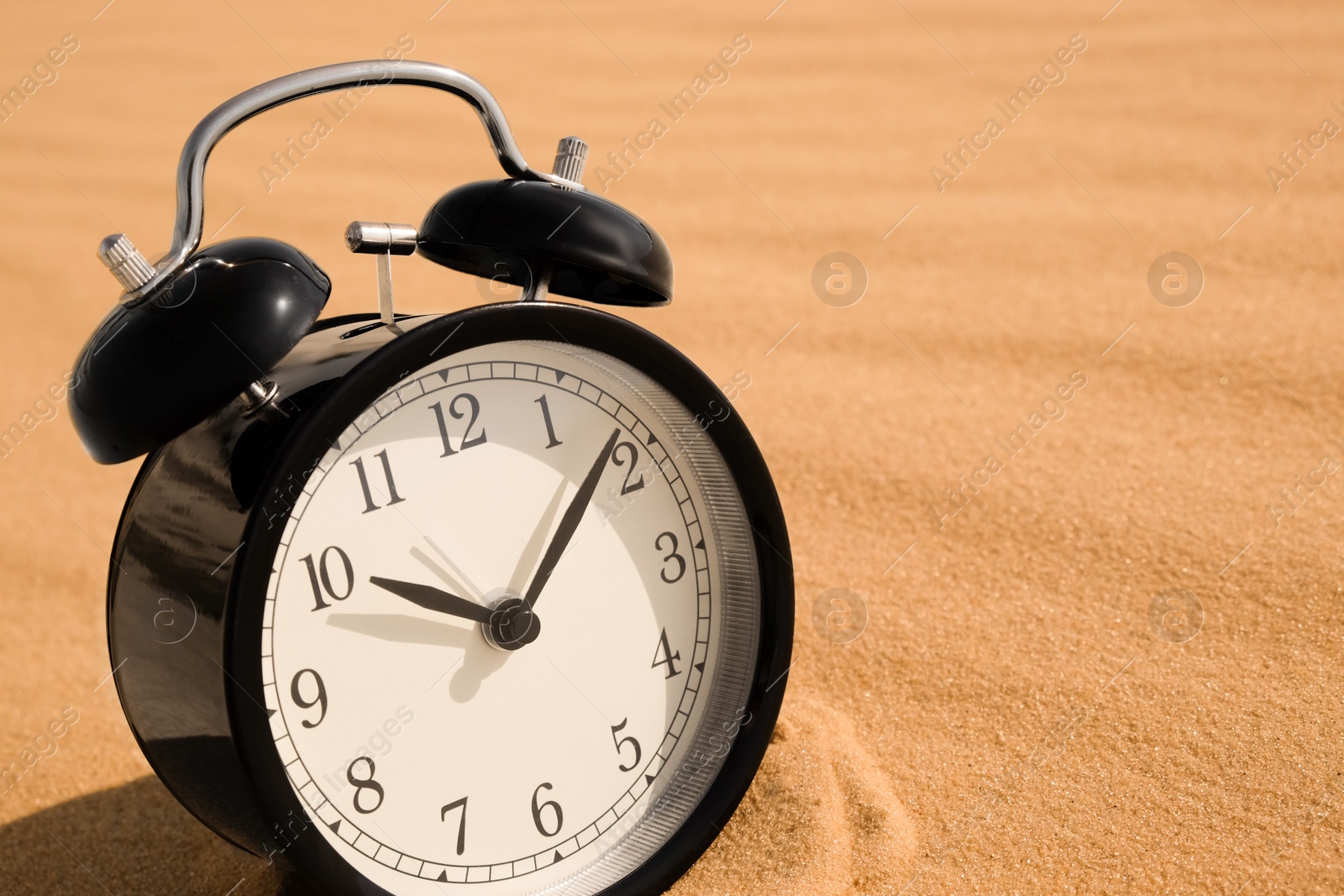 Black alarm clock on sand in desert, closeup. Space for text Photo of Black alarm clock on sand in desert, closeup. Space for text