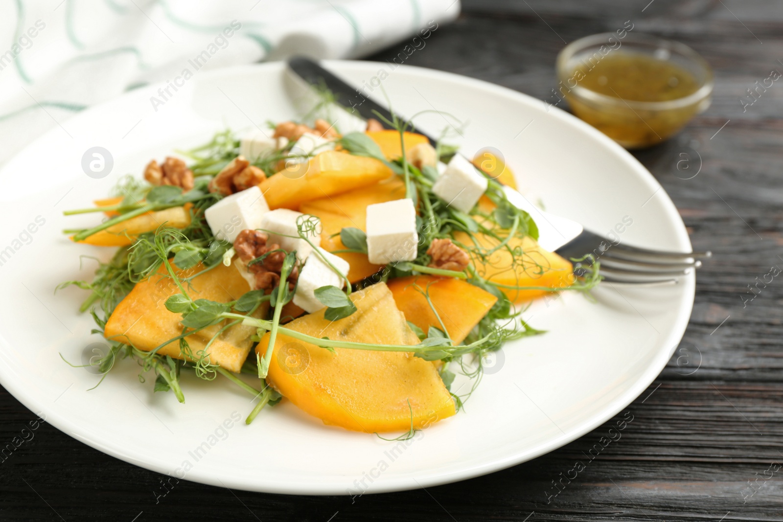 Delicious persimmon salad with feta cheese and walnuts on wooden table, closeup Photo of Delicious persimmon salad with feta cheese and walnuts on wooden table, closeup
