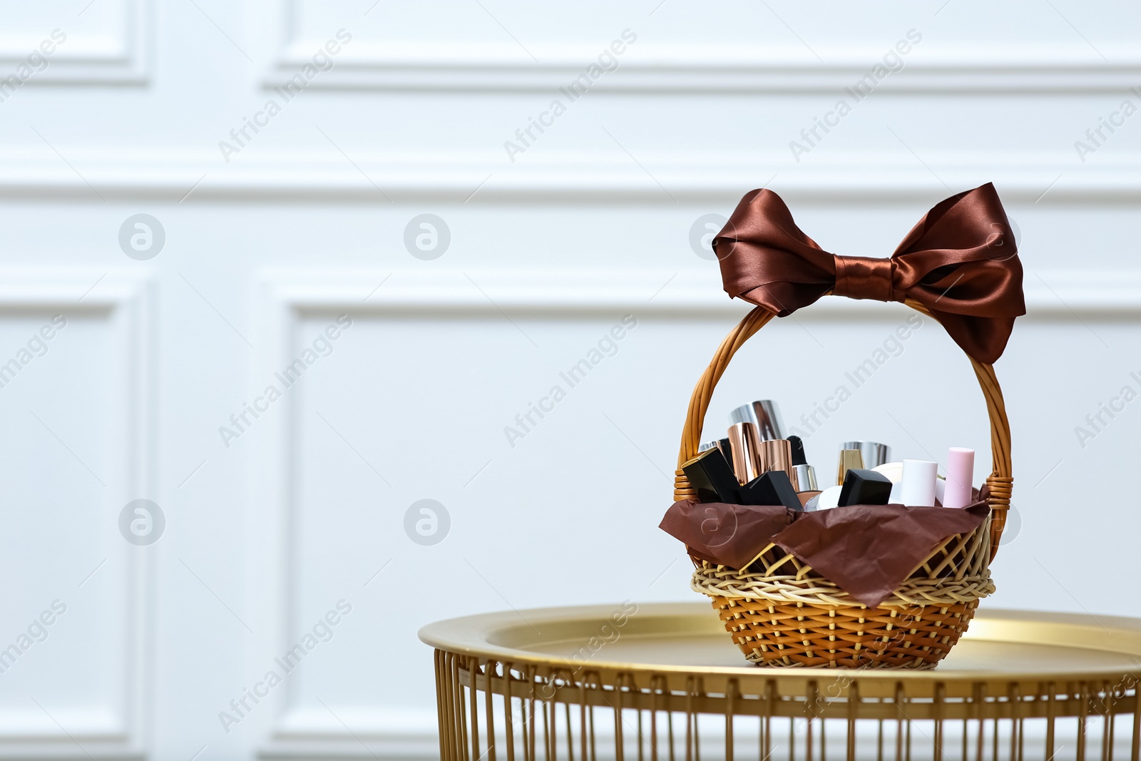 Gift set in wicker basket on golden table near white wall. Space for text Photo of Gift set in wicker basket on golden table near white wall. Space for text