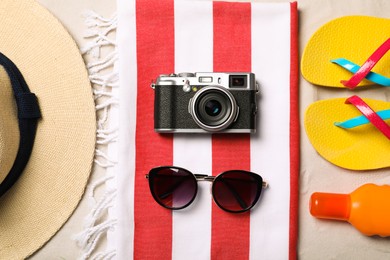 Hat, sunglasses, camera, sunscreen, beach towel and flip flops on sand, flat lay Photo of Hat, sunglasses, camera, sunscreen, beach towel and flip flops on sand, flat lay
