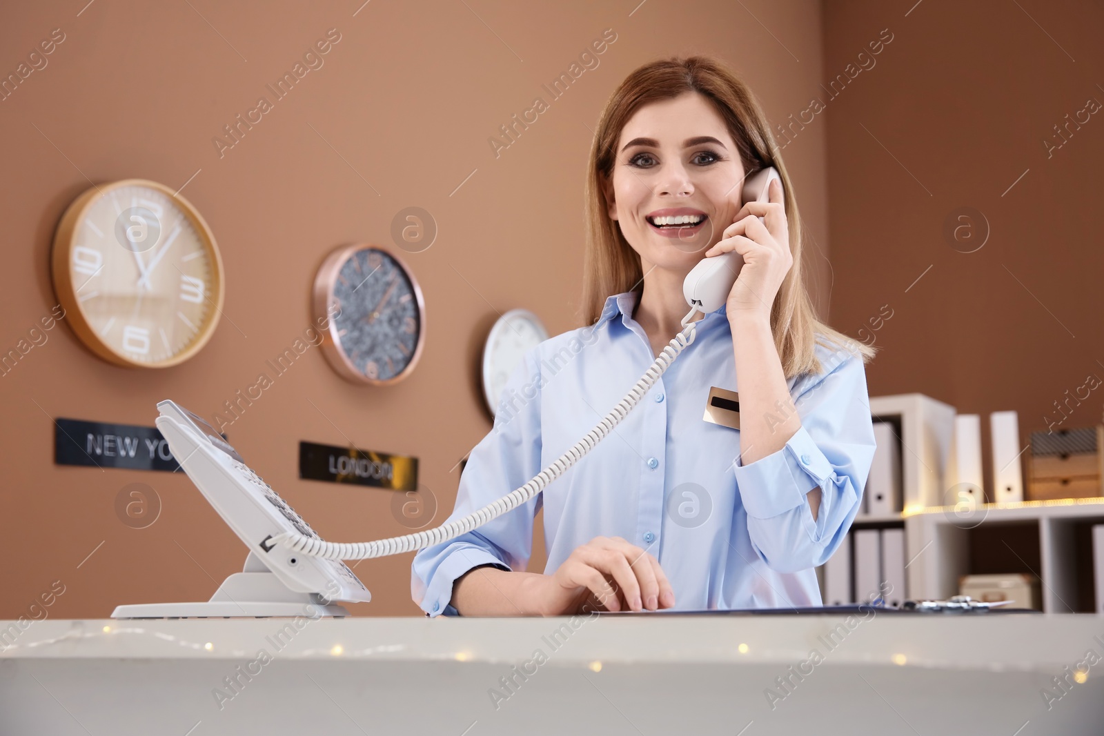 Female receptionist talking on phone at hotel check-in counter Photo of Female receptionist talking on phone at hotel check-in counter