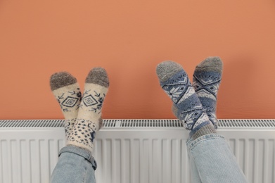 Couple warming legs on heating radiator near color wall, closeup Photo of Couple warming legs on heating radiator near color wall, closeup