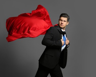 Businessman in superhero cape taking suit off on grey background Photo of Businessman in superhero cape taking suit off on grey background