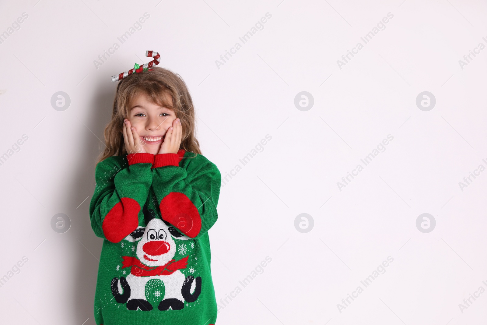Cute little girl in green Christmas sweater smiling against white background Photo of Cute little girl in green Christmas sweater smiling against white background