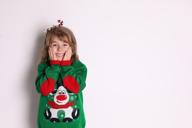 Cute little girl in green Christmas sweater smiling against white background Photo of Cute little girl in green Christmas sweater smiling against white background