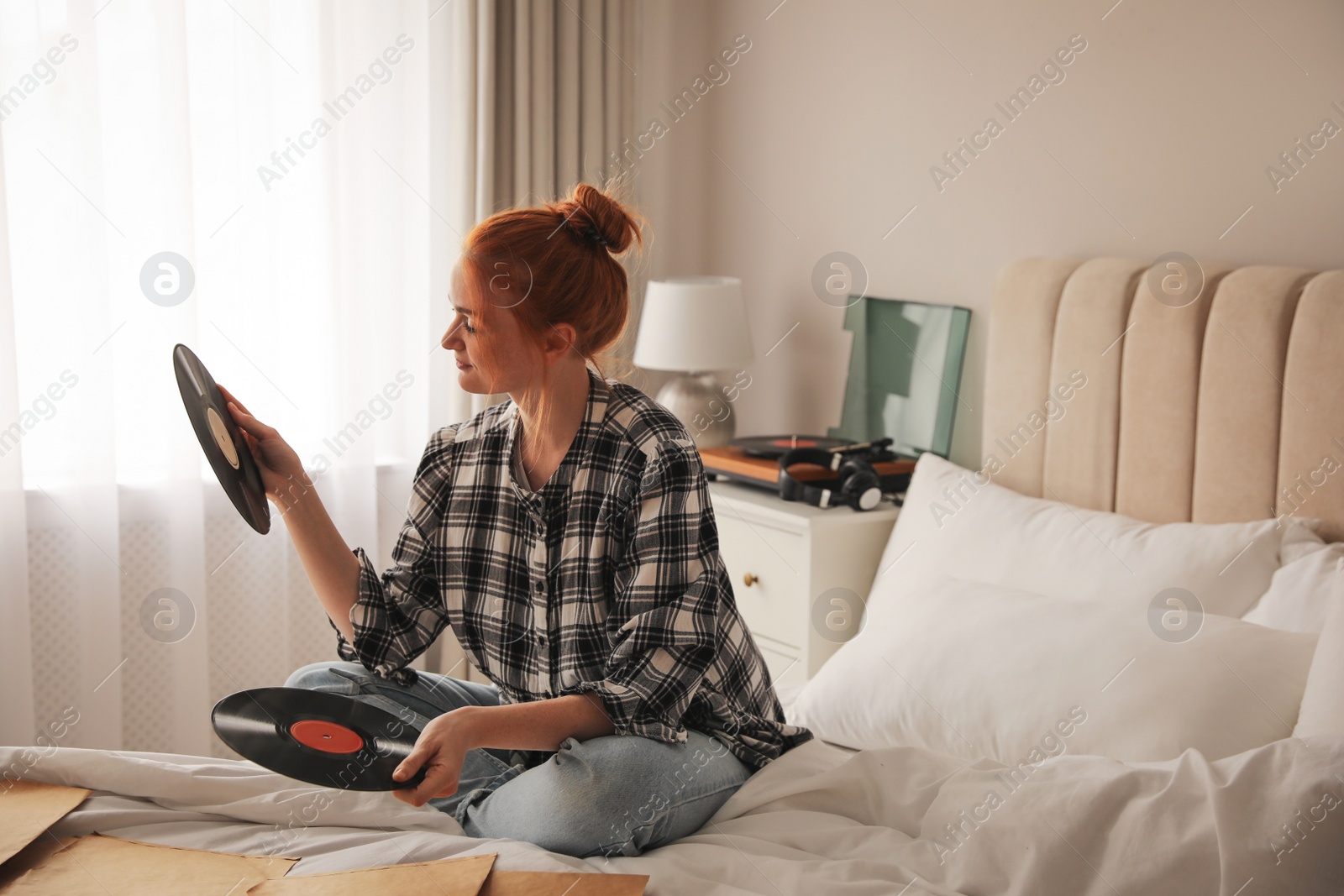 Young woman choosing vinyl disc to play music with turntable in bedroom Photo of Young woman choosing vinyl disc to play music with turntable in bedroom