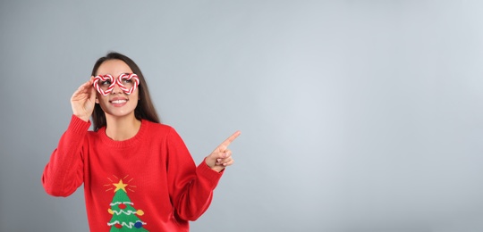 Young woman in Christmas sweater and party glasses on grey background, space for text Photo of Young woman in Christmas sweater and party glasses on grey background, space for text