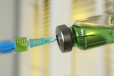 Photo of Filling syringe with medication from vial against blurred background, closeup. Vaccination and immunization