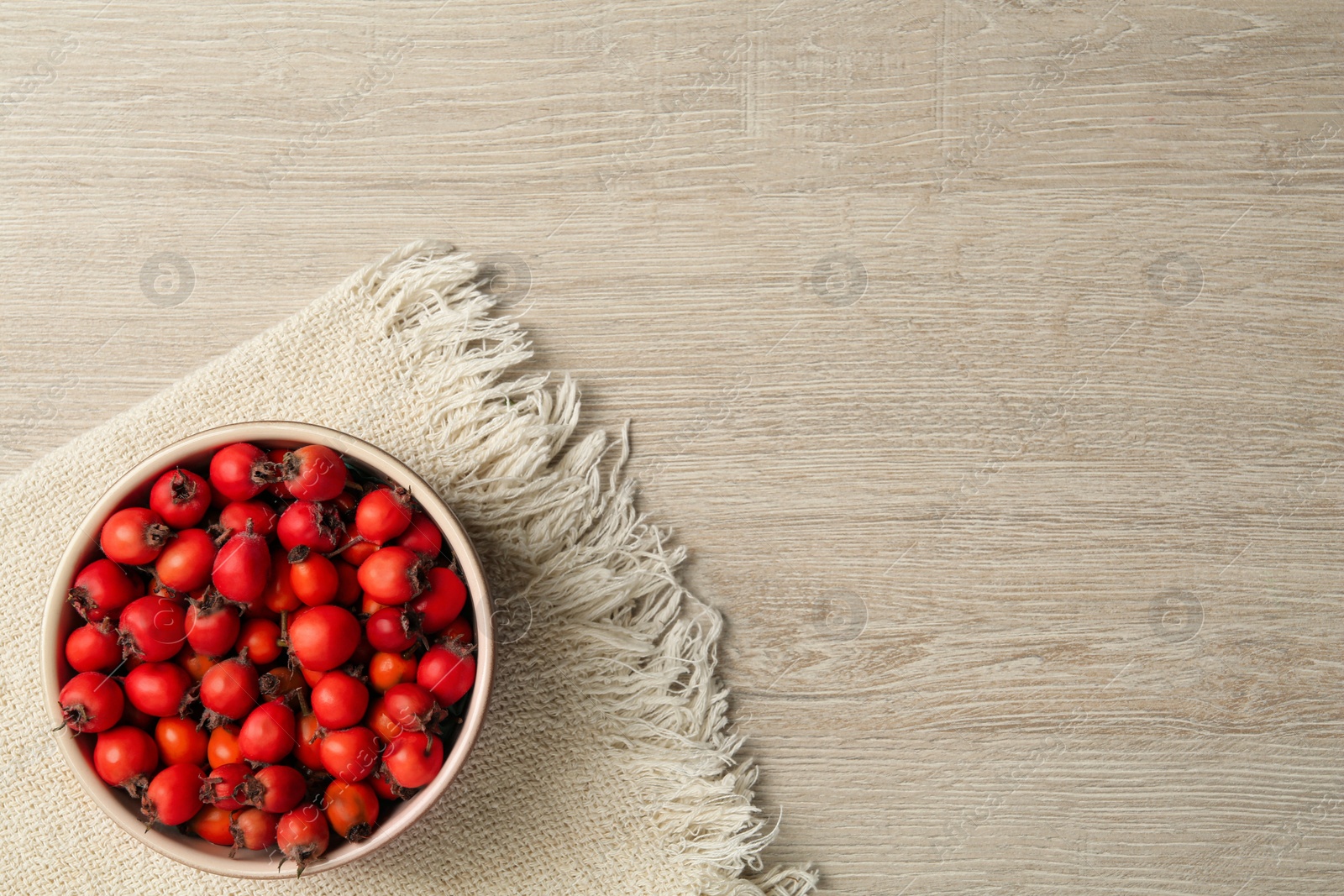 Ripe rose hip berries in bowl on wooden table, top view. Space for text Photo of Ripe rose hip berries in bowl on wooden table, top view. Space for text