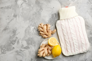 Photo of Hot water bottle with knitted cover and natural remedies from cold on grey stone background, flat lay. Space for text