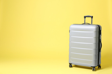 Stylish grey suitcase on yellow background. Space for text Photo of Stylish grey suitcase on yellow background. Space for text