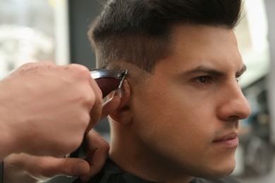 Photo of Professional barber making stylish haircut in salon, closeup
