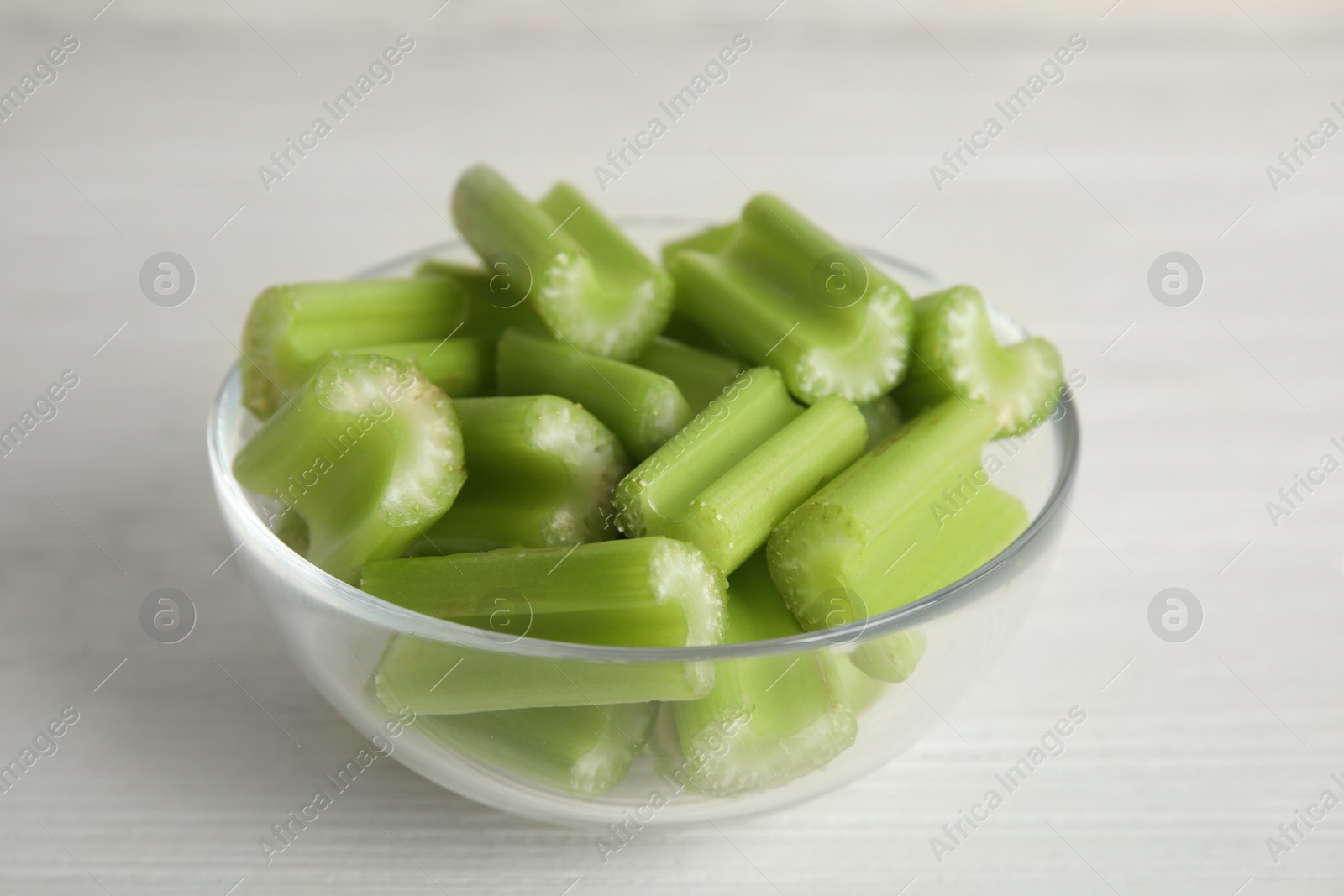 Cut celery in glass bowl on white wooden table, closeup Photo of Cut celery in glass bowl on white wooden table, closeup
