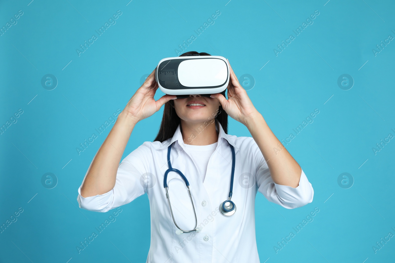 Female doctor using virtual reality headset on light blue background Photo of Female doctor using virtual reality headset on light blue background