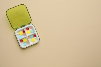 Photo of Plastic box with different pills on beige background, top view. Space for text